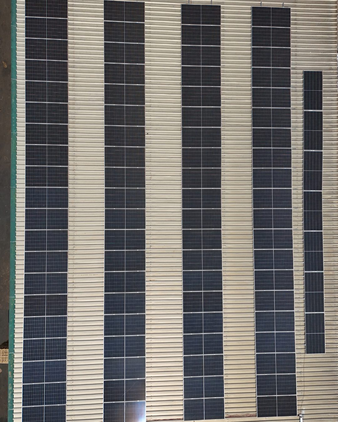 Vista aérea do telhado metálico ondulado da CRMORENO com fileiras verticais de painéis solares.